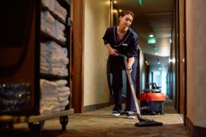 Young cleaning lady vacuuming hotel hallway.